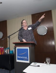 A woman standing at a podium, telling a story, point up to the left