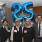 Six staff members posing in front of a blue balloon in the shape of a 25