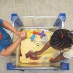 Two children are playing with toys in a box of sand