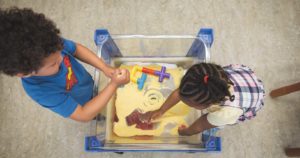 Two children are playing with toys in a box of sand