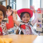 A young boy and girl, wearing cowboy hats, are having fun with their hands in the air